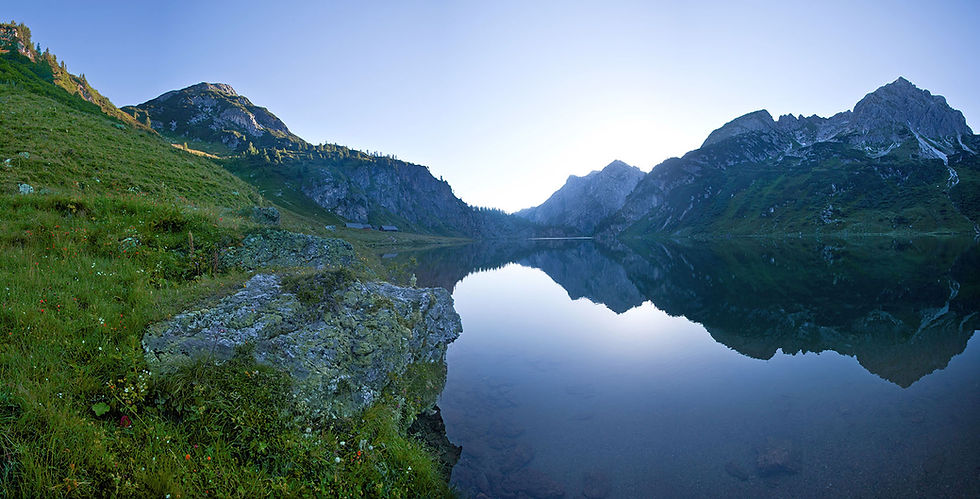 See im ruhigen, blauen Dämmerungslicht mit Fels im linken Vordergrund. Bevor die Sonne die Berggipfel berührt, dominiert das diffuse, kühle Licht der blauen Stunde.
