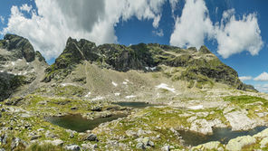 Epische Totalaufnahme der majestätischen Nordwestflanke des Hochwildstellen-Massivs (2.747 m). Dunkler, schroffer Fels bricht abwechselnd mit leuchtend grünen Grasbändern auf. Der Vordergrund zeigt die ersten alpinen Ausläufer.
