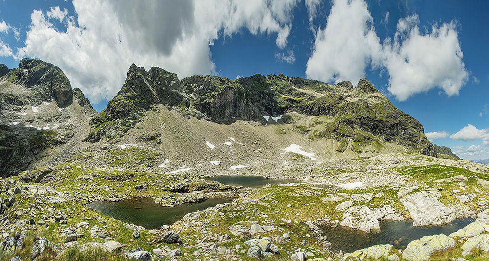 Epische Totalaufnahme der majestätischen Nordwestflanke des Hochwildstellen-Massivs (2.747 m). Dunkler, schroffer Fels bricht abwechselnd mit leuchtend grünen Grasbändern auf. Der Vordergrund zeigt die ersten alpinen Ausläufer.