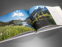 Geöffneter Bildband "Made in Austria" mit einer großformatigen Panorama-Fotografie des Dachsteinmassivs und Gosausees in Oberösterreich auf einer blühenden Bergwiese.