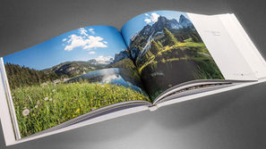 Geöffneter Bildband "Made in Austria" mit einer großformatigen Panorama-Fotografie des Dachsteinmassivs und Gosausees in Oberösterreich auf einer blühenden Bergwiese.