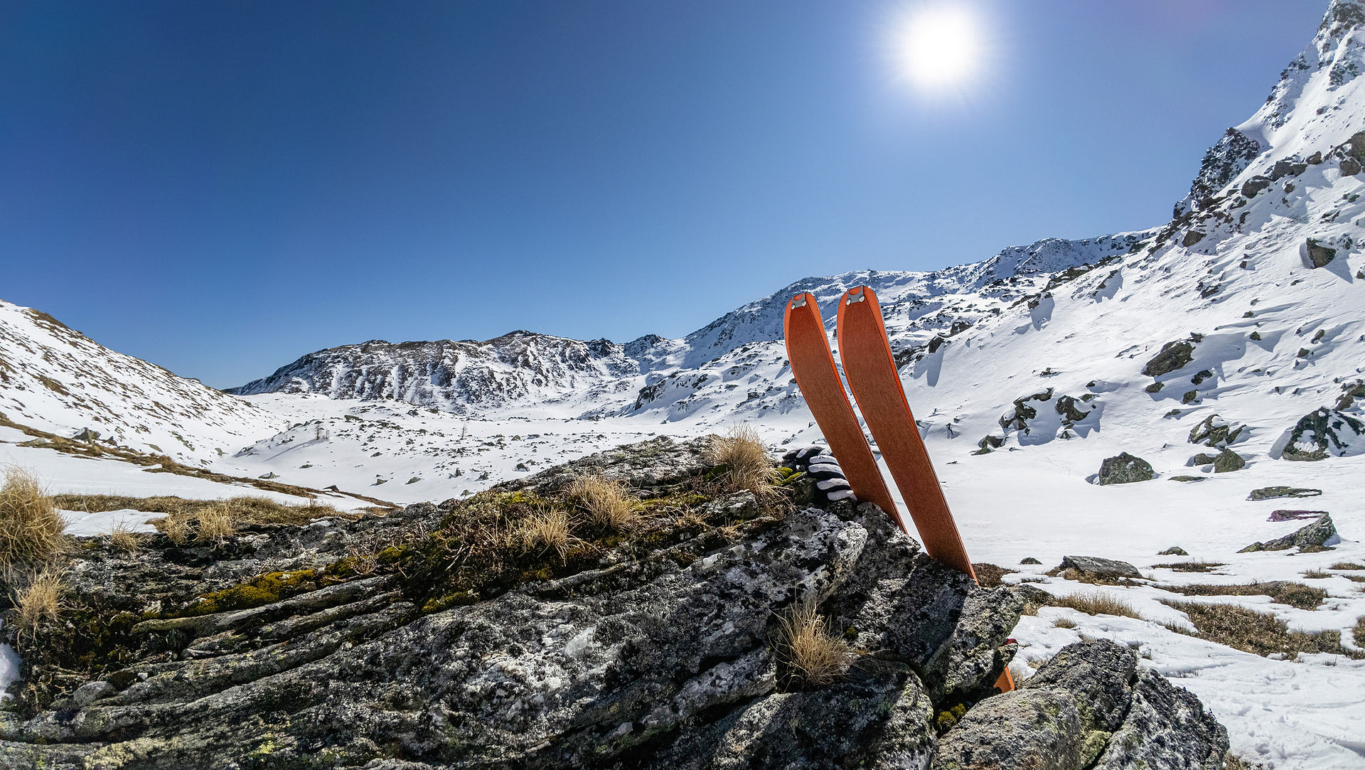 Blick auf die schneebedeckte Landschaft in den Seetaler Alpen, mit Ski, die auf einem Felsen ruhen, und strahlend blauem Himmel im Hintergrund.