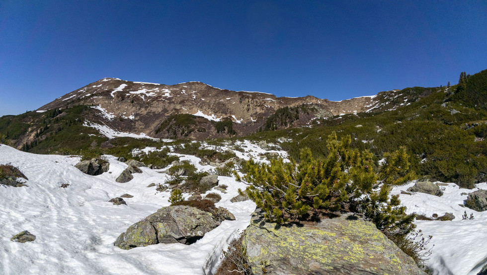 Blick auf die Berge der Planneralm, wo der Schnee schmilzt und die Vegetation sichtbar wird, unter einem strahlend blauen Himmel.