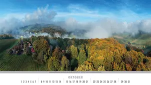 Blick von oben auf bunte Reben und Herbstwälder an der Südsteirischen Weinstraße mit aufsteigenden Nebelschwaden im Oktober