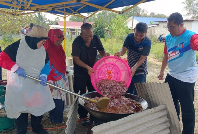 Anggota KEADILAN dan masyarakat setempat bergotong royong memasak daging korban