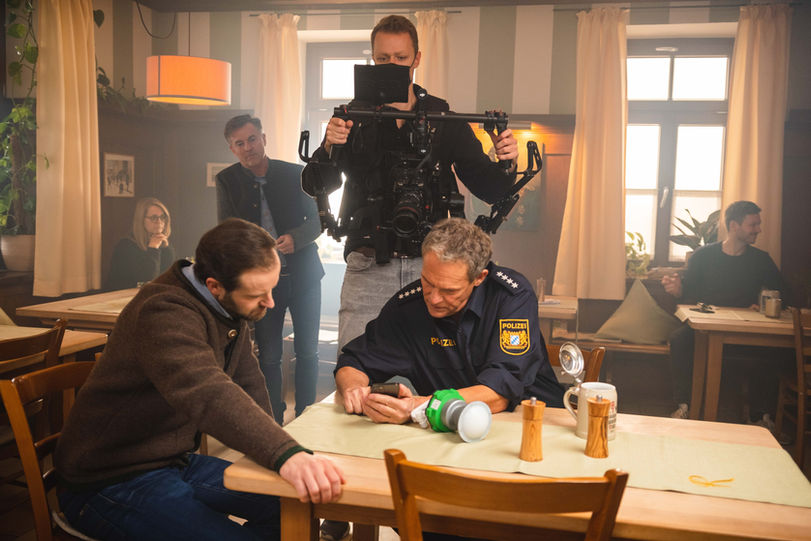 Ein Kameramann filmt in einem Restaurant, eine Szene aus IMAGEFILM. Männer am Tisch.
