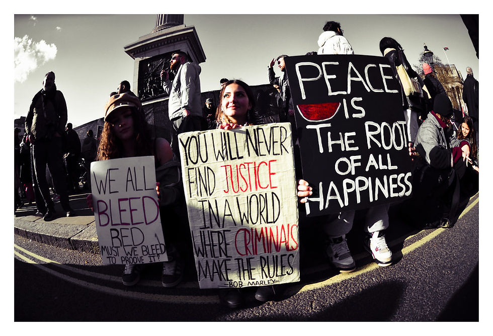 Protest with people holding signs reading "We All Bleed," "You Will Never Find Justice," and "Peace is the Root of All Happiness" outside. Together Alliance, London, March 2026