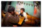 Two women chat at a bar table under 70th birthday bunting, with green curtains and balloons in a cozy dim lounge.