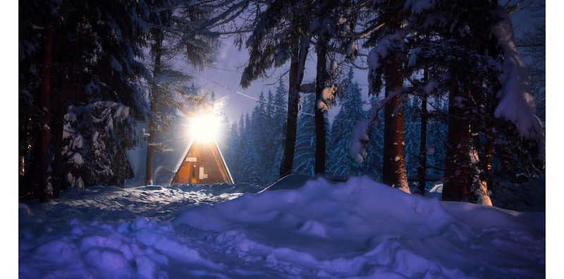 Log cabin in the woods in a winter wonderland setting at night.