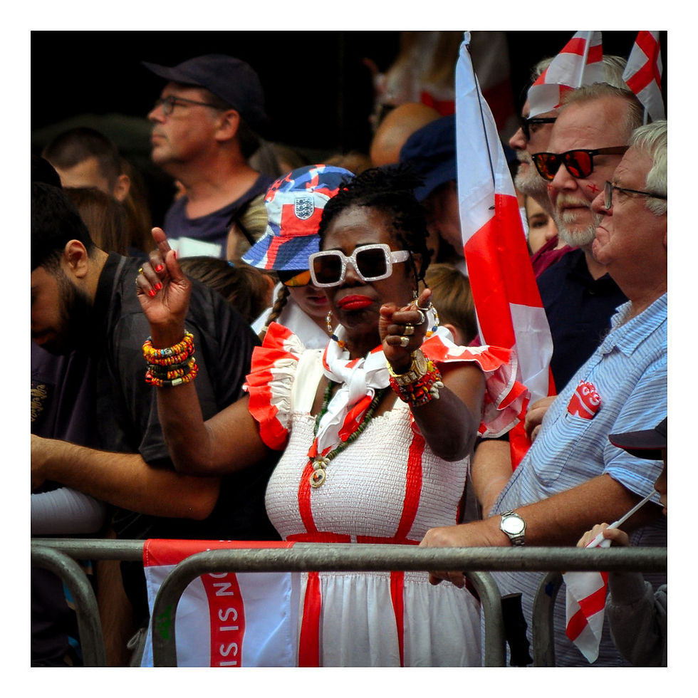 Crowd of people with English flags, a woman in white and red, wearing sunglasses and colourful bracelets, gestures energetically. Festive mood. Celebrations of England Women's Euro 2025 win at the Victory Parade