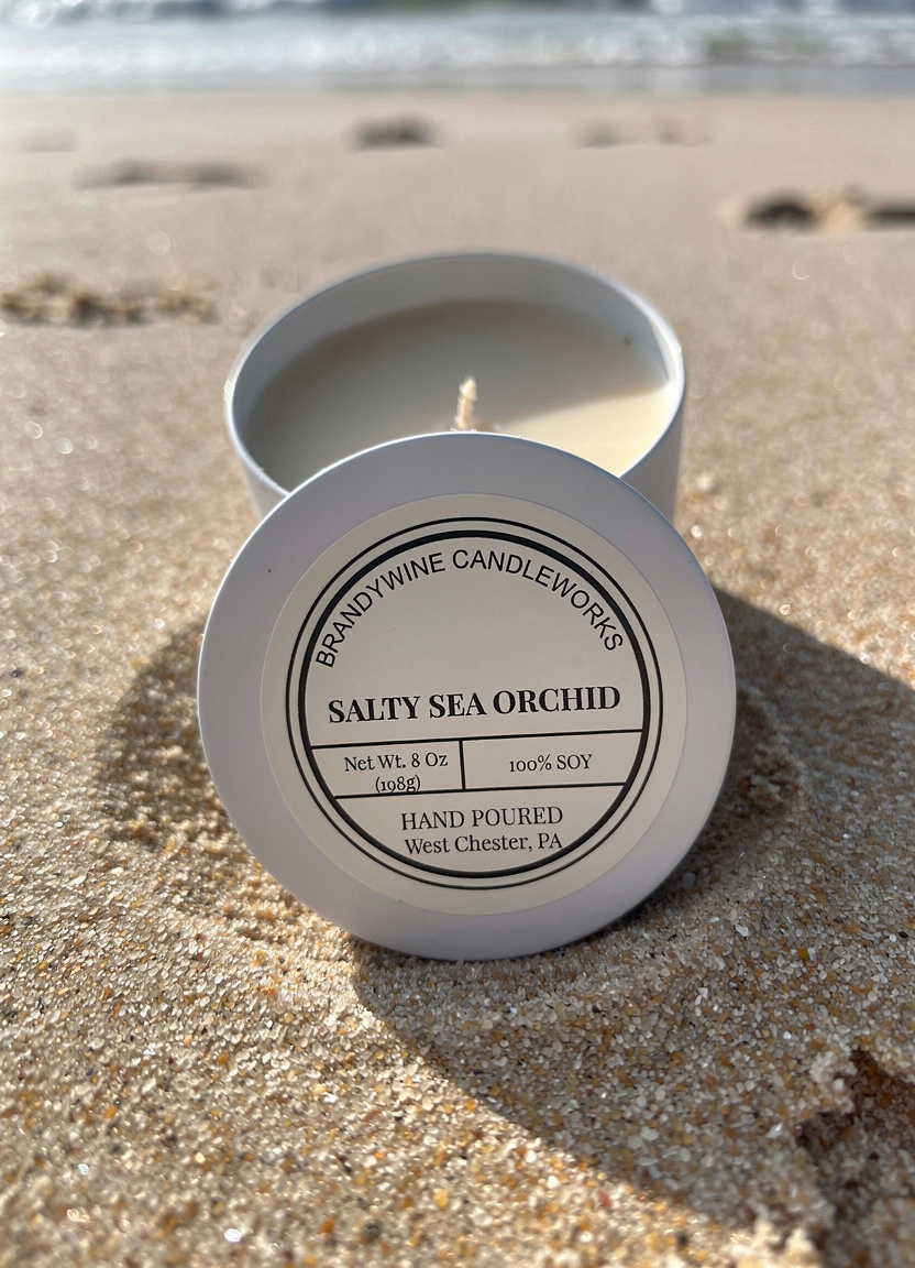 Salty Sea Orchid soy candle tin, open on sandy beach