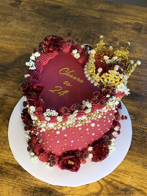 Heart-shaped cake with gold crown and text: Cheers to 24. A party cake.