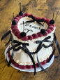 White cake with Aries text, cherries, and black ribbons for celebration.