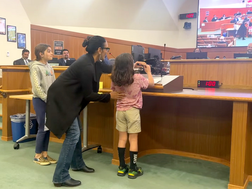 Seema Patel adjusts the microphone for her 8 year old son Remy before he gives a public comment in support of bike lanes at a San Mateo City Council meeting. His 10 year old big sister looks on in pride.