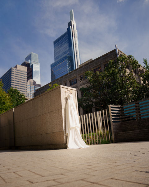 Wedding dress hanging outdoors with city buildings in background.