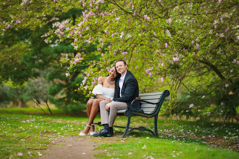 Couple sitting on bench under flowering tree in park.