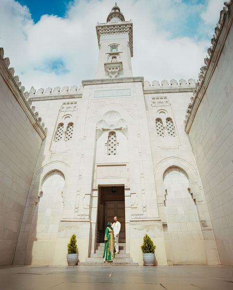 Couple standing at entrance of large ornate building with tall archways.