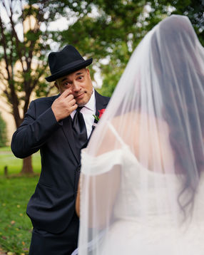Groom in suit and hat wiping tear while looking at bride in veil during first look