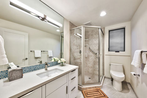 A well-designed guest bathroom featuring a corner glass shower, modern vanity with an integrated sink, and a clean mix of mosaic and neutral tiling.