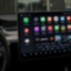 Car dashboard with a large touchscreen displaying various colorful app icons. Steering wheel visible on the left. Modern tech vibe.