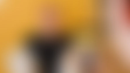 Nainen ottaa videota miehestä, joka seisoo keltaisen taustan edessä jauhopussi kädessä
