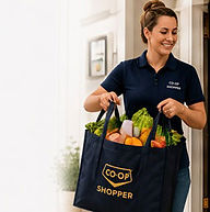Delivery operator at a front door holding a Co-Op Shopper tote filled with groceries, with a soft fade to a light neutral background on the left for clean website placement.