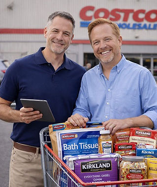 Two middle-aged male grocery operators standing in a Costco warehouse parking lot with a cart full of Kirkland items and bulk groceries, reviewing orders on a tablet.