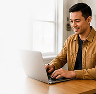 Man working on a laptop at a desk in a bright home setting, with a soft fade to light neutral on the left side for clean website text placement.
