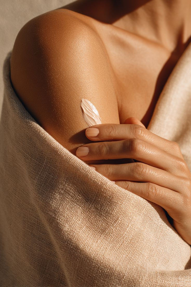 Een vrouw die in zachte ochtendlicht een body cream aanbrengt op haar arm, in een minimalistische badkamersetting