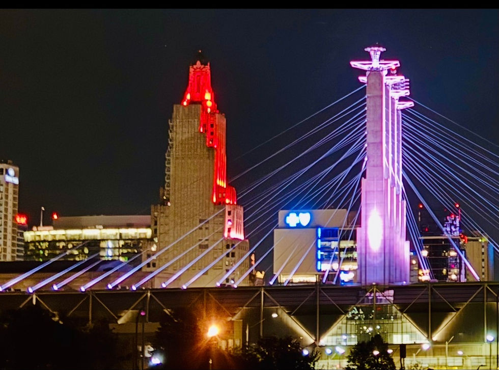 Bartle Hall pylons and cables lit at night beside the red-lit Power and Light Building in downtown Kansas City.