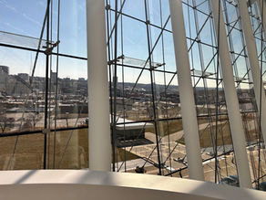 White structural columns and a monumental glass wall frame the Kansas City skyline from inside a modern atrium.