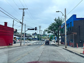 West Bottoms street with red and blue industrial buildings, overhead lines and the KC Wheel beyond the intersection.