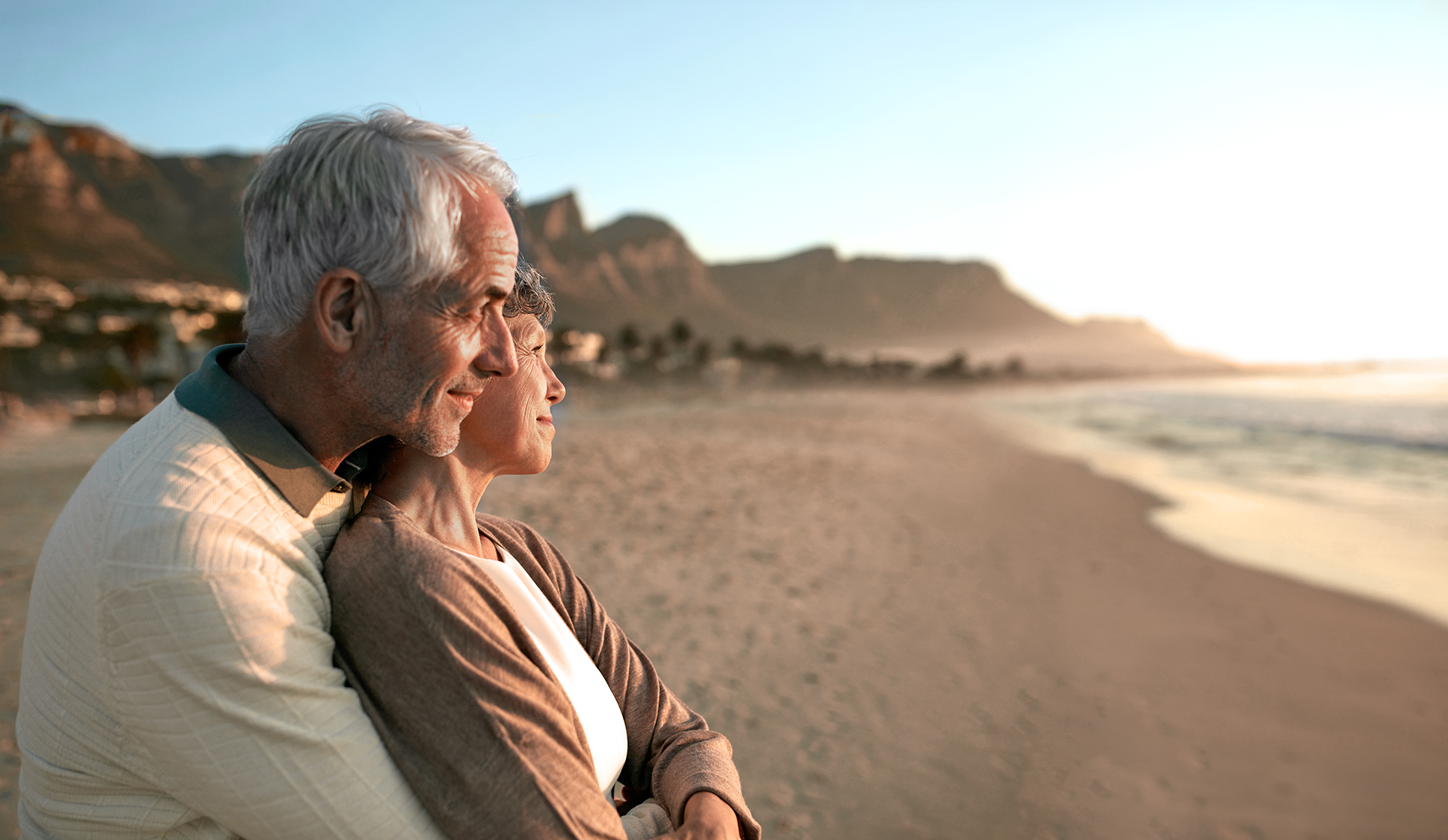 Senior couple holds each other while watching the sunset on the beach as was their homework from couple's session