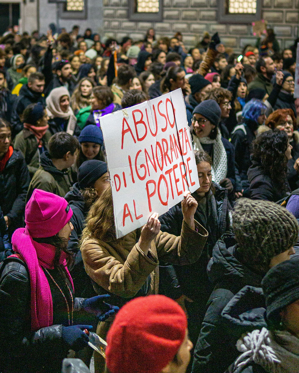 Un'affollata manifestazione notturna in piazza. Al centro, una persona solleva un cartello bianco con la scritta in rosso e nero "ABUSO DI IGNORANZA AL POTERE". Molti partecipanti indossano berretti invernali - https://unsplash.com/it/foto/QQ-qYVtv9UM