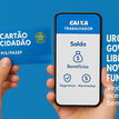"Pessoa segurando um Cartão Cidadão em foco, com celular ao lado exibindo o aplicativo da Caixa Econômica Federal."