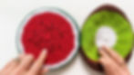 Hands pointing to the embroidered seeds on a round crocheted potholder that looks like a slice of watermelon and a slice of kiwi.