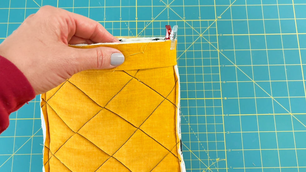 Hand holding a yellow quilted fabric with sewing clips against a green cutting mat with a grid pattern.
