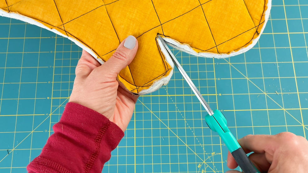 Hands in red sleeves cutting yellow quilted fabric with teal scissors on a blue grid mat. Geometric pattern visible.