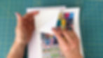 Hands peeling the backing off a sheet of sticker paper filled with book covers.