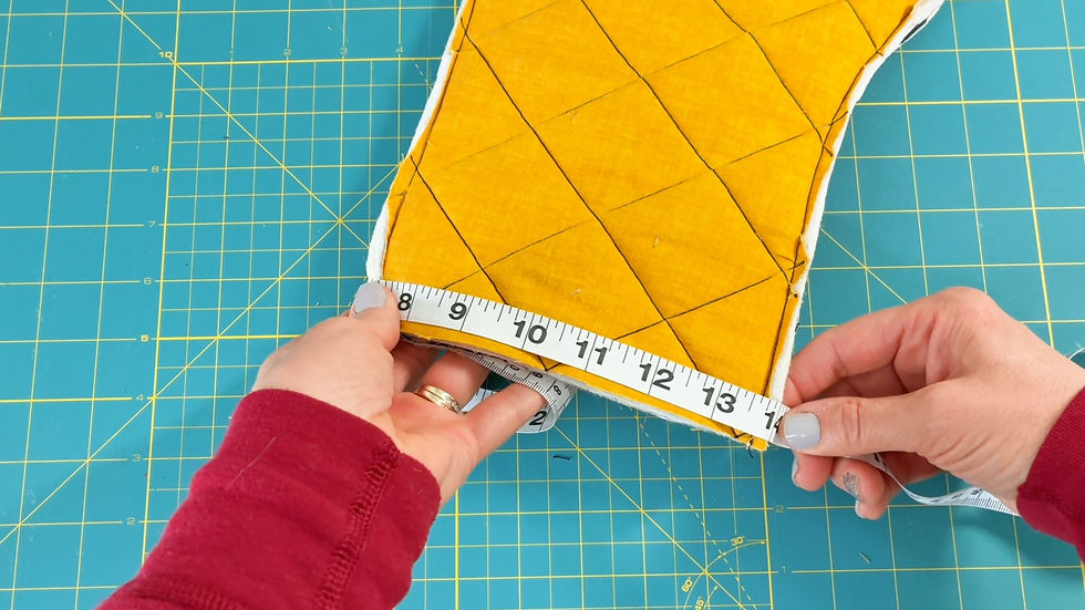 Hands measuring yellow quilted fabric with tape measure. Green grid cutting mat background. Fabric has diamond pattern.