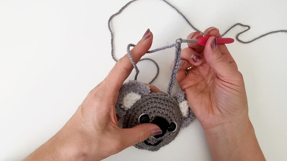 Hands holding a crocheted koala Christmas ornament and attaching a haning loop using chain sttiches.