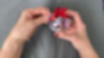 Hands tacking down the end of a ribbon tail onto the top of a clear fillable ornament filled with book covers.