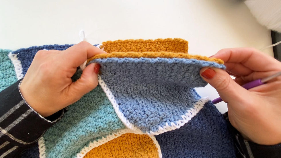 Hands showing how to hold the crocheted blocks to join them together to make a baby blanket by single crocheting.