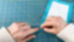 Hands folding the corner of a piece of blue fabric.