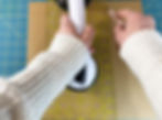 Hands holding a fabric ruler and Cricut TrueControl blade on a cutting mat to cut through chipboard.