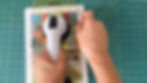 Hands using a sewing ruler and Cricut TrueControl blade to cut out book covers from a piece of sticker paper adhered to foam core board.