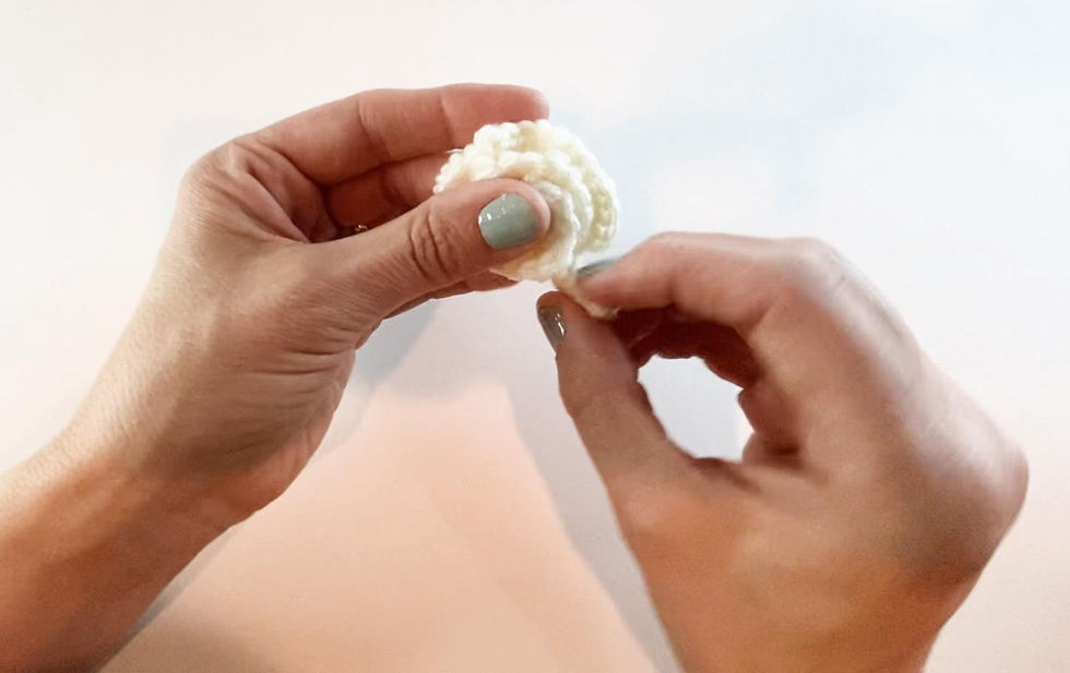 Hands unrolling a white crocheted curlicue to form a whipped cream topping for a marshmallow mug hat.