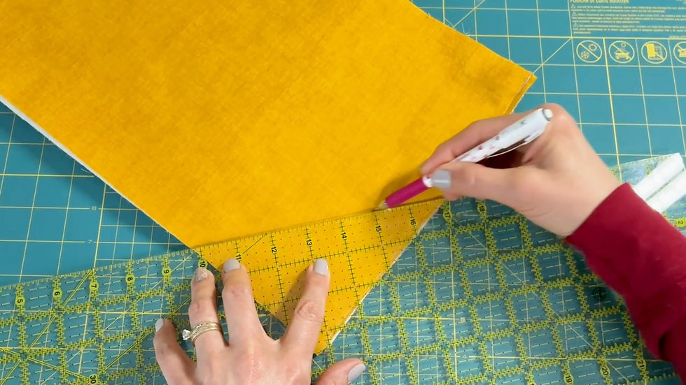 Hands measuring yellow fabric with a clear ruler and marking with a pink pen on a green cutting mat with grid lines.