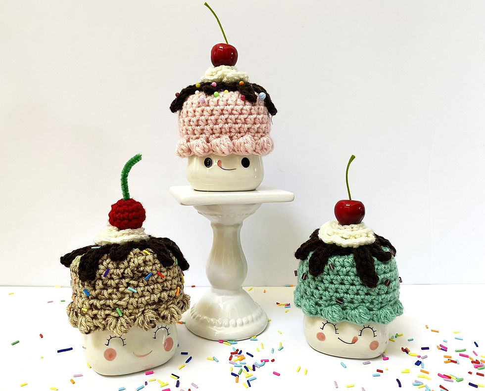 Three marshmallow mugs wearing crocheted hats that look like ice cream.