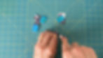 Hands using a Cricut TrueControl blade to cut excess foam core board off a book cover printed on sticker paper.